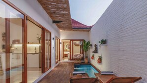 A modern indoor pool area with wooden loungers, a small pool, and a kitchen visible through glass doors. - Senna Villa (Munggu)