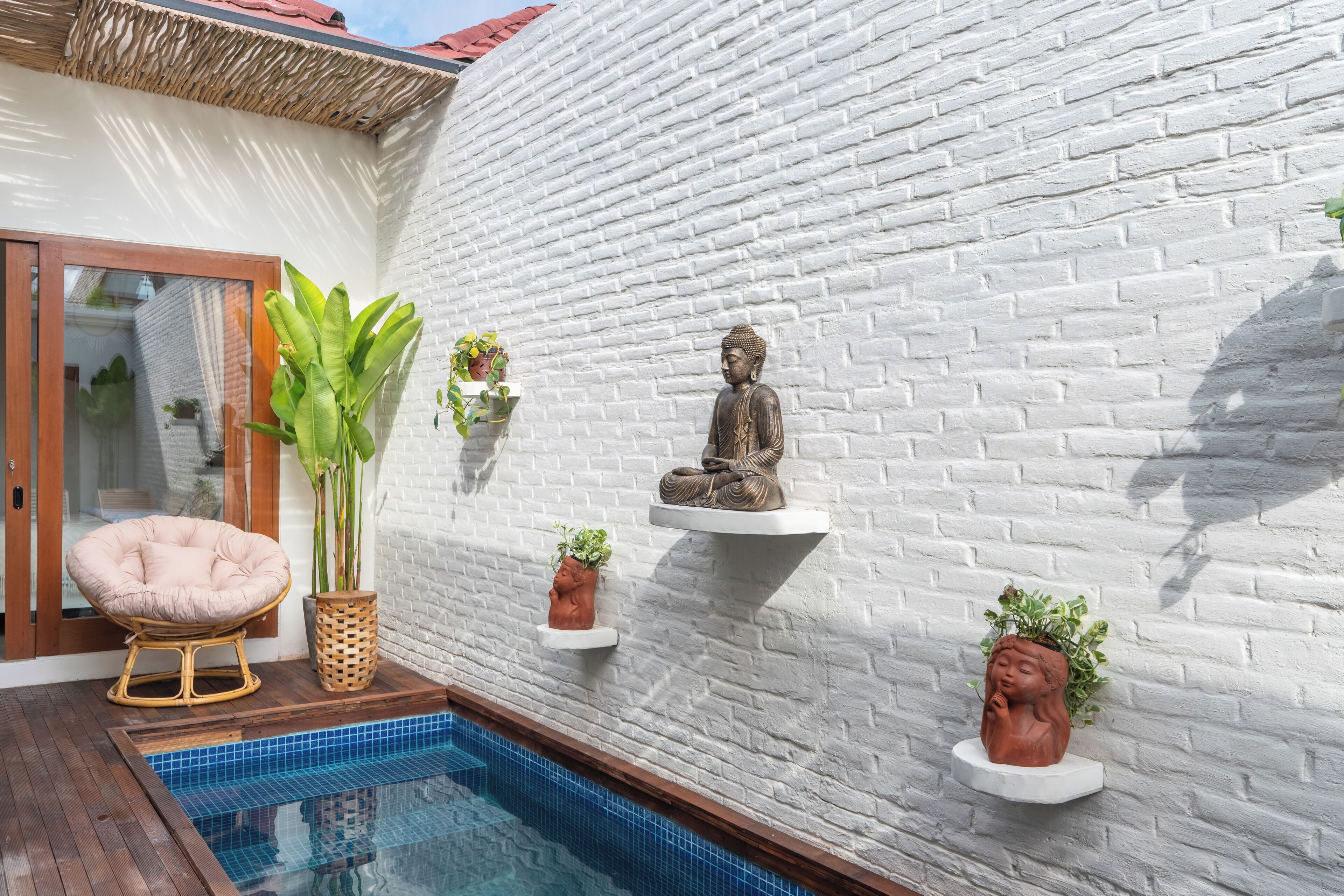 Ein Poolbereich mit einer weißen Backsteinmauer, einer Buddha-Statue und Kübelpflanzen.