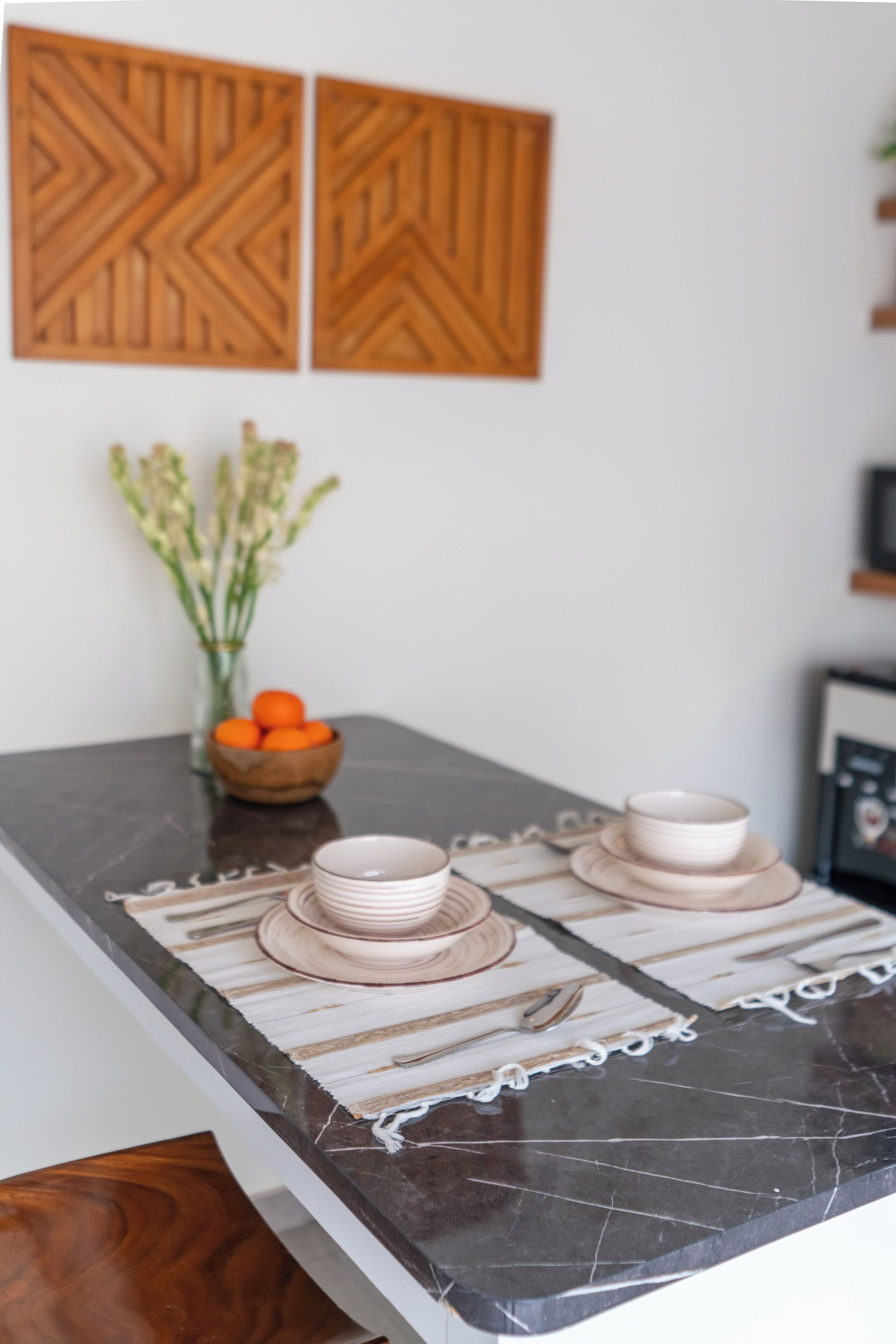 Un comptoir de cuisine surmonté d’un plateau en marbre, un saladier en bois rempli d’oranges et un vase avec des fleurs.
