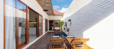 A modern outdoor patio with wooden furniture, a pool, and a white brick wall.
