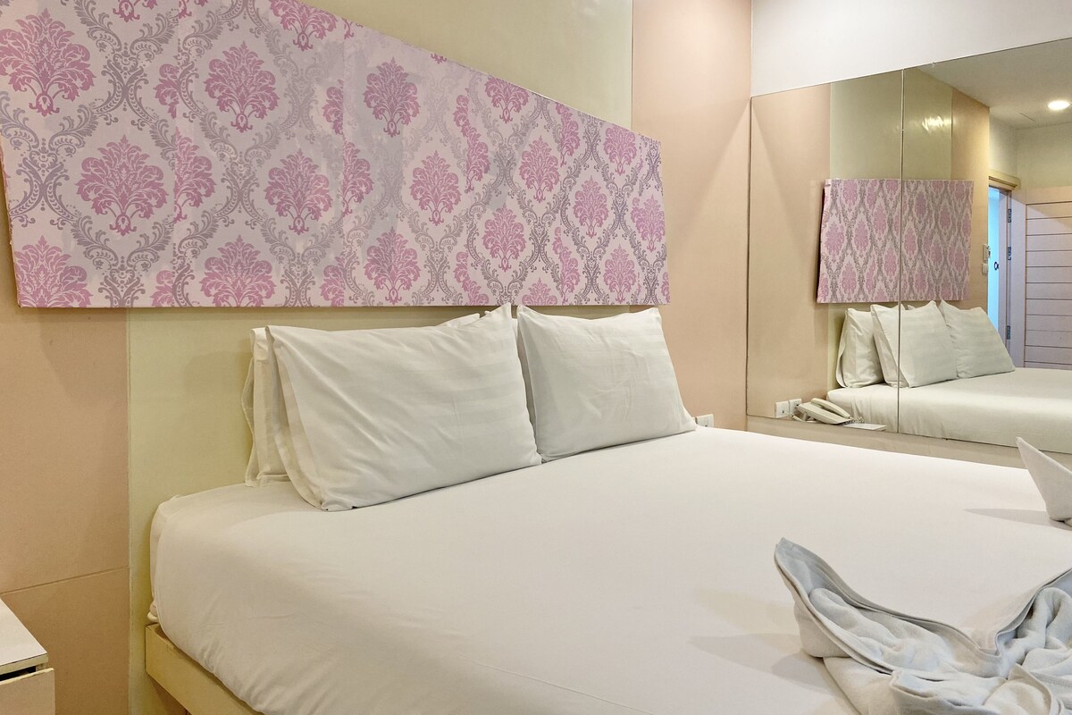 Hotellihuone, jossa on suuri sänky, valkoiset vuodevaatteet, peili ja kuviollinen tapetti.