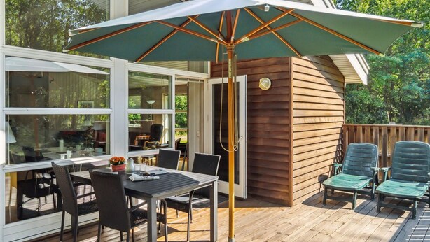 Une terrasse extérieure avec une table et des chaises, un grand parasol et une rambarde en bois.