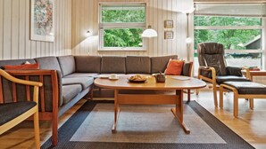 Un salon chaleureux avec un canapé, une table basse et un fauteuil. Il y a deux fenêtres équipées de stores, une lampe et un tableau encadré au mur.