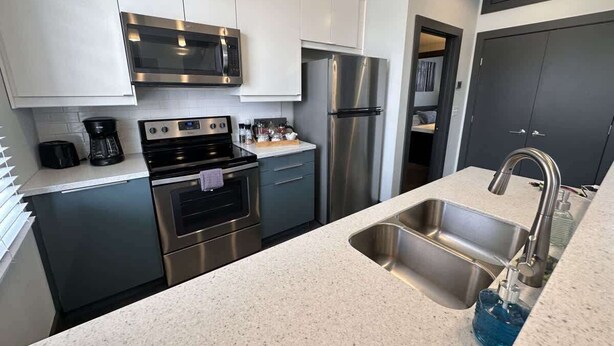 A modern kitchen with stainless steel appliances, a double sink, and a countertop with a coffee maker. - Stay Roanoke | Walkable Downtown Rooftop Apt (Roanoke)