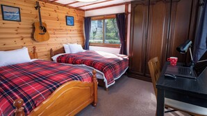 Ein Zimmer mit zwei Holzbetten, einem Schreibtisch mit einem Laptop, einer Gitarre an der Wand und einem Fenster mit Vorhängen.