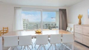 Un comedor moderno con una mesa grande, sillas blancas y vistas de la ciudad a través de amplias ventanas.