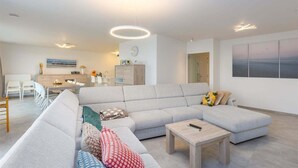 Una sala moderna con un sofá modular, una mesa de centro de madera y un comedor con sillas blancas.