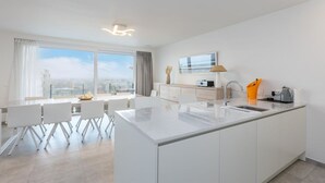 Una cocina moderna con una isla grande, armarios blancos y vistas a la ciudad a través de amplios ventanales.