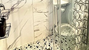 Eine Duschkabine mit Marmorwand und einem gemusterten Vorhang.