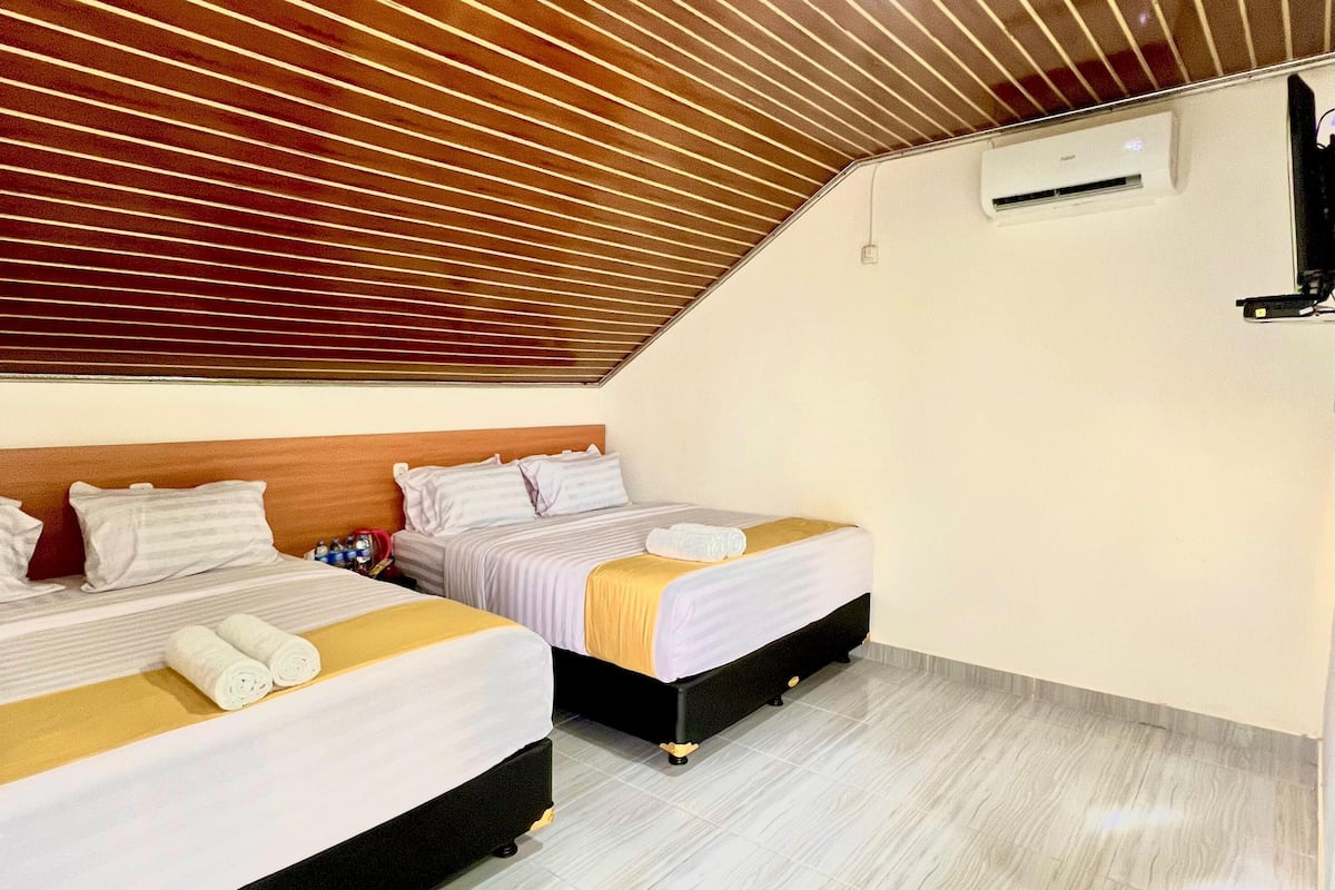 A hotel room with two beds, wooden slatted ceiling, white walls, and a tiled floor.