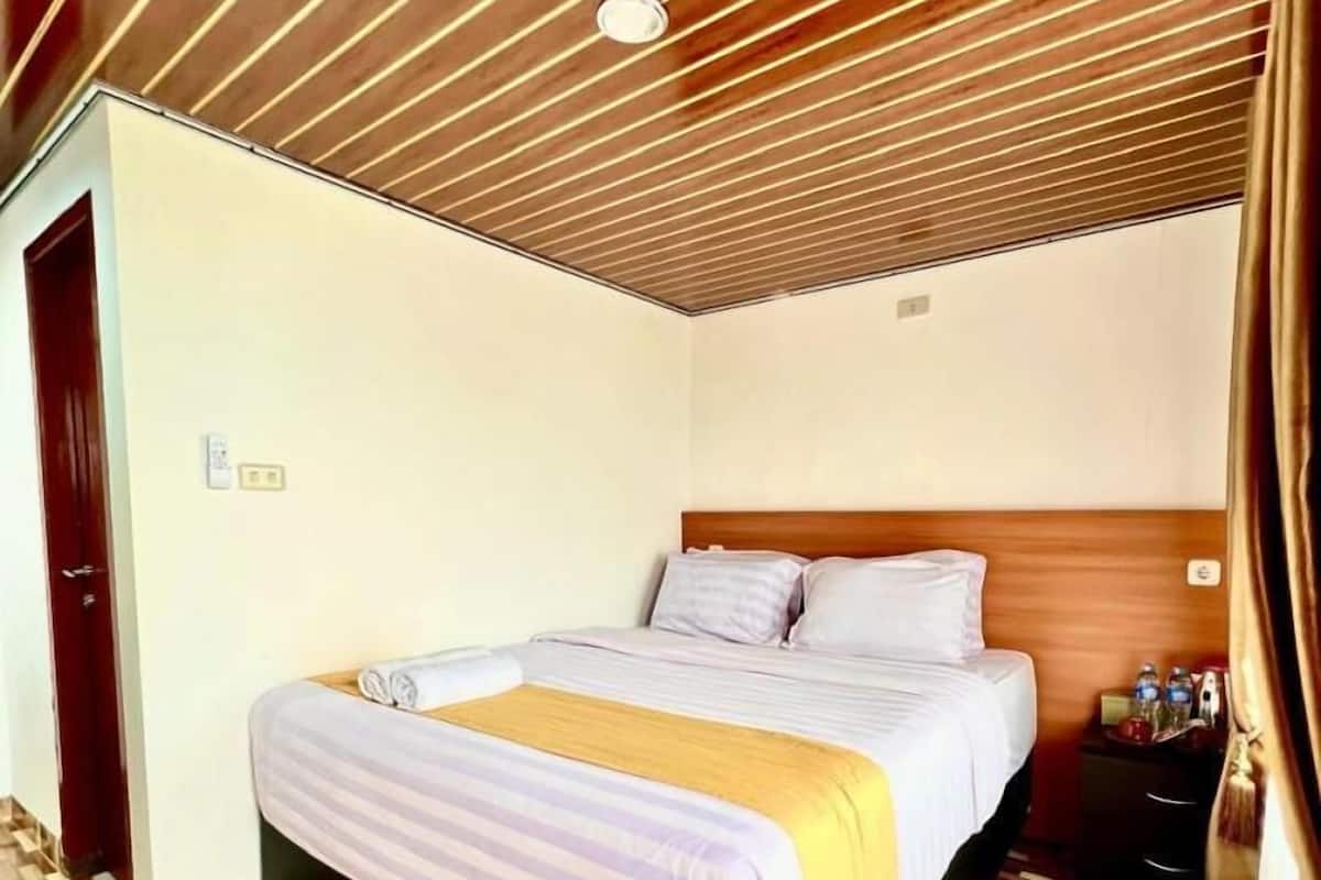 A bedroom with a wooden slatted ceiling, a bed with a striped bedspread, and a patterned wooden floor.