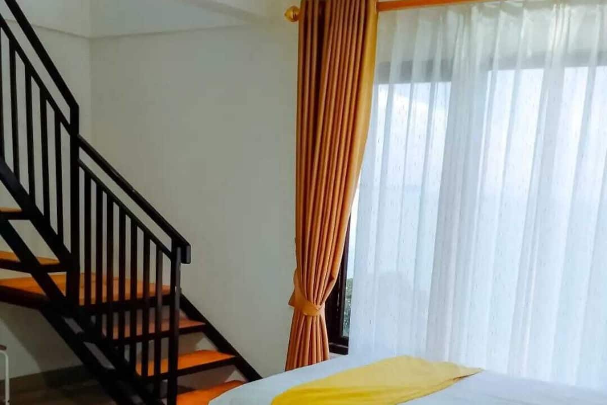 A hotel room with a staircase, a bed with a yellow blanket, and a window with curtains.
