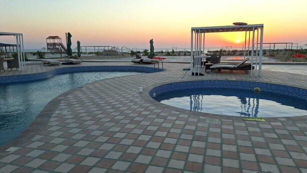 A pool area with lounge chairs and a pergola at sunset. - Sugardunes Resort (Al Khaluf)