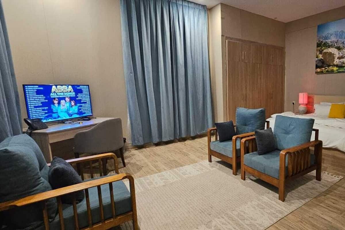 A hotel room with a bed, a desk with a computer, a chair, a coffee maker, and a painting on the wall.