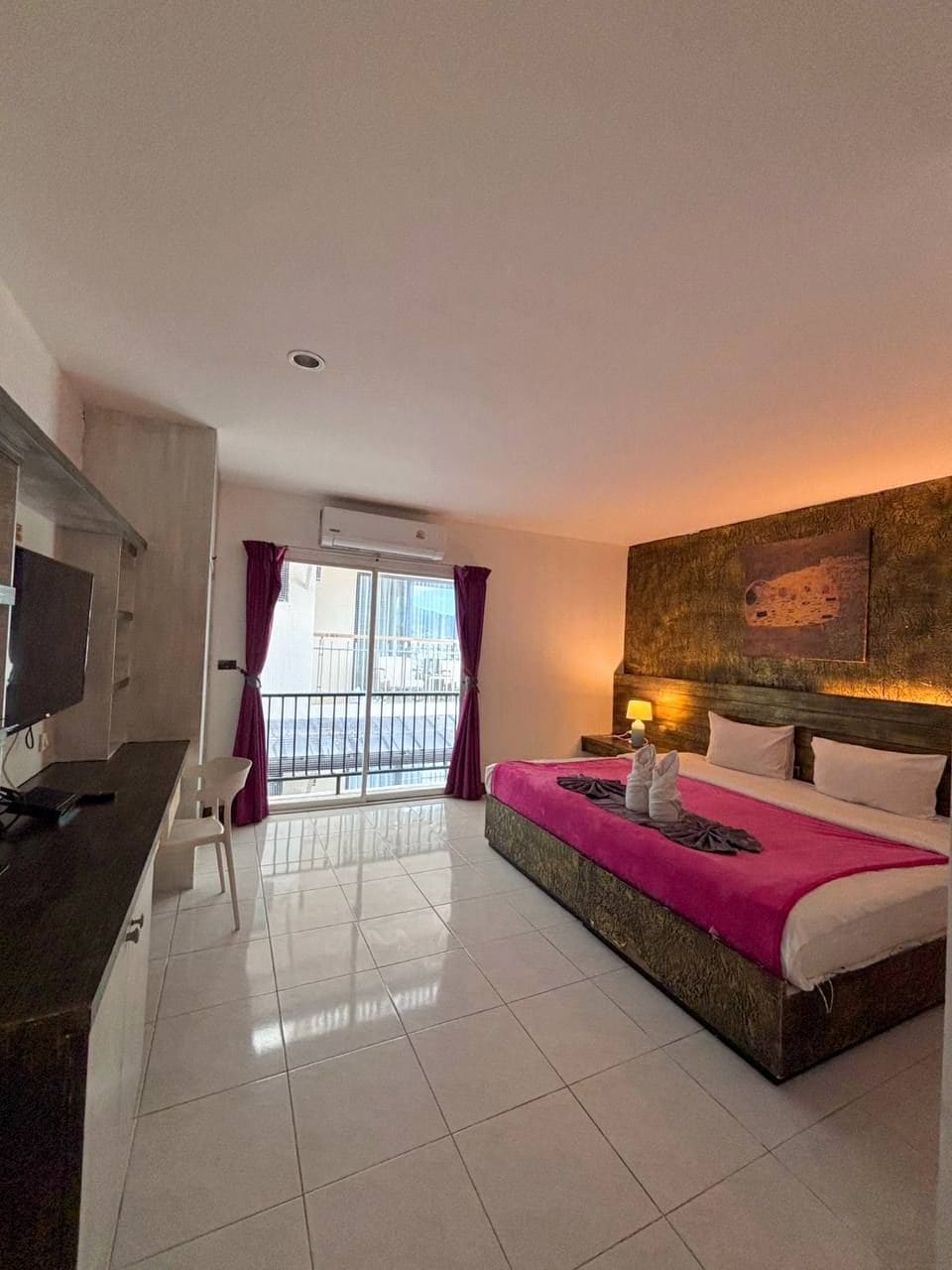 Ein Hotelzimmer mit Bett, Schreibtisch, Stuhl, Fernseher und einem Balkon mit Vorhängen.