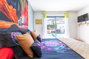 A bedroom with a bed, pillows, a TV, a painting, and a view of the outside. - Guest Room "La Catalane" Direct Pool Access, Outdoor Lounge, Wi-Fi (Treilles)