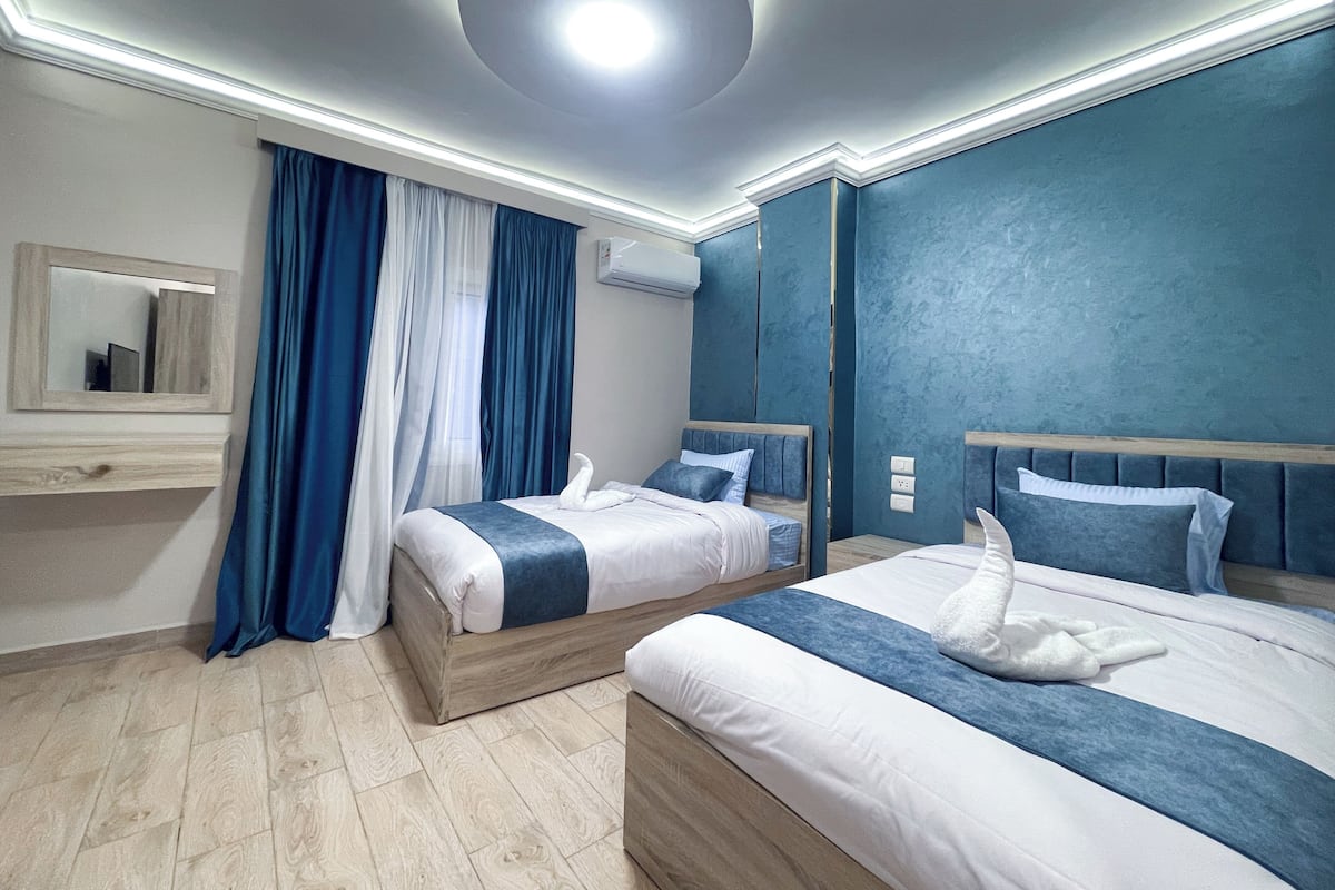 A hotel room with two beds, a mirror, an air conditioning unit, and a ceiling light.