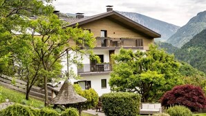 Uma casa de dois andares com varanda, cercada por vegetação exuberante e montanhas.