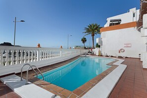 A swimming pool with a white fence, a palm tree, and a building with a white facade.