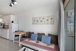 A compact living space with a kitchenette, a sofa with patterned throw, and a wall-mounted artwork.