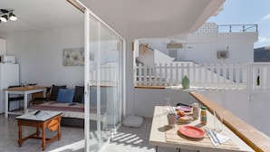 Ein helles Zimmer mit Esstisch, einer Couch, einem kleinen Tisch mit Lampe und einer Treppe, die zu einer oberen Ebene führt.
