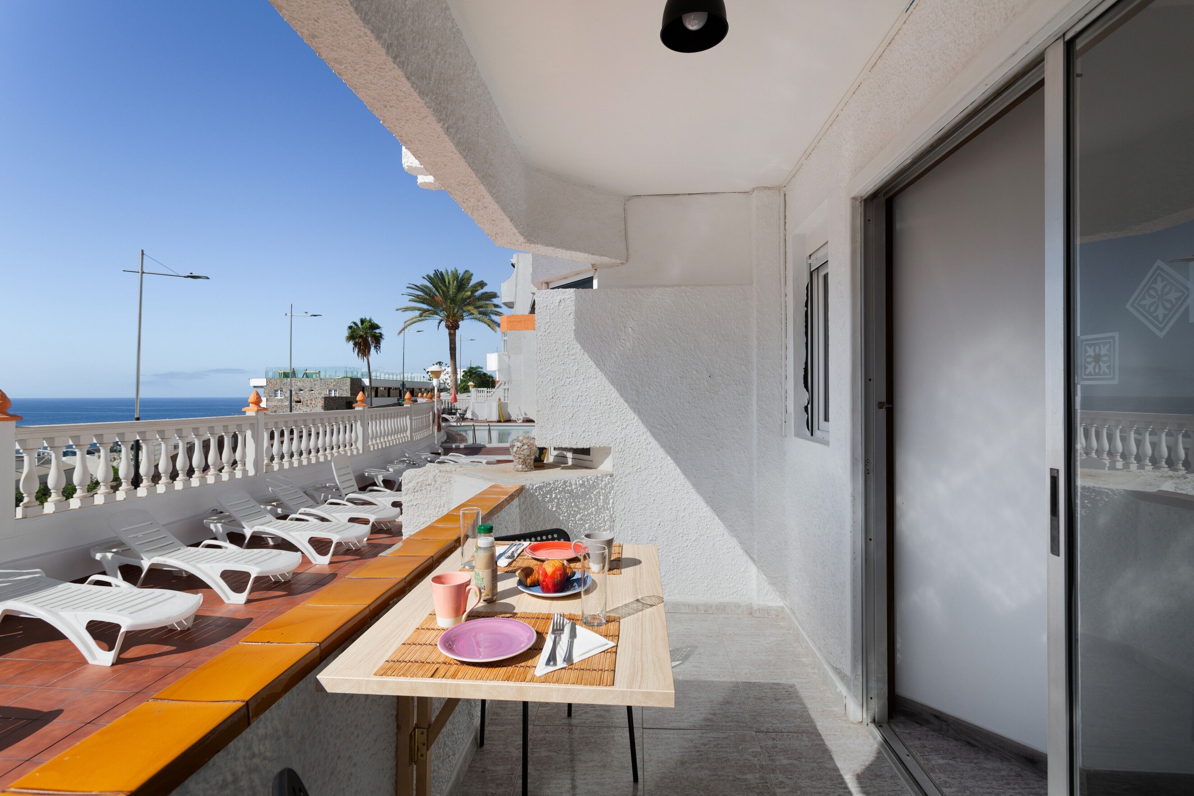A balcony with a dining table set, chairs, and a view of the sea.