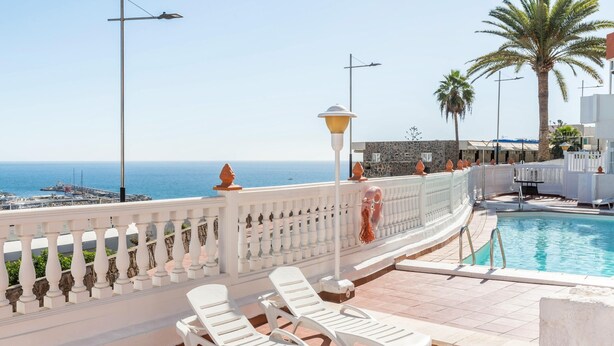 Ein Poolbereich mit weißen Liegestühlen und Blick auf das Meer.