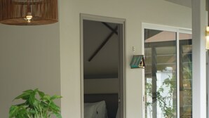 Zona junto a la piscina con una mesa y sillas de madera, una planta en maceta y vista a un dormitorio a través de un vidrio.