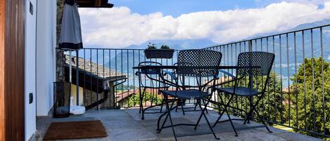 A balcony with a table and chairs, a small plant, and a view of mountains.