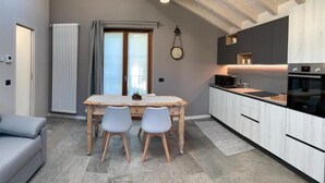 A modern kitchen with a wooden dining table and chairs, a built-in oven, and a large window with curtains.