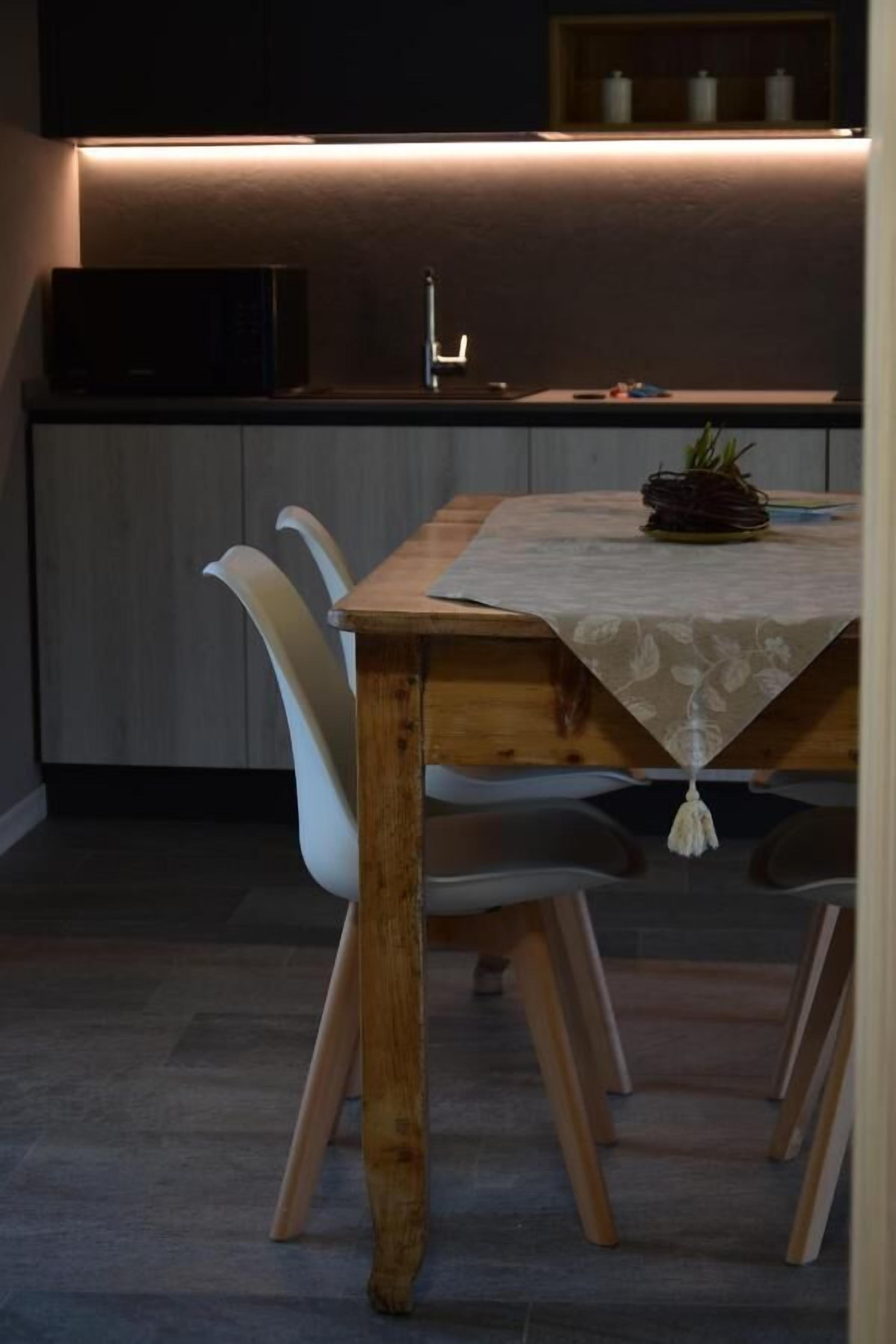 A modern kitchen with a wooden dining table, white chairs, and a built-in oven.