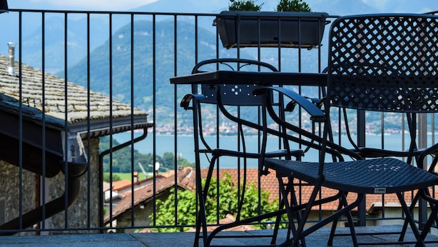 A balcony with a metal railing, a chair, a small table, and a planter with plants.