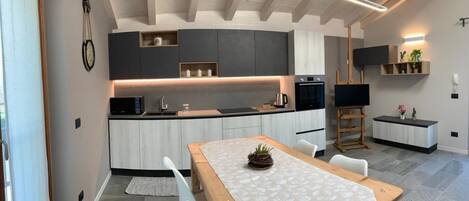 A modern kitchen with a wooden table and chairs, built-in appliances, and a pendant light.