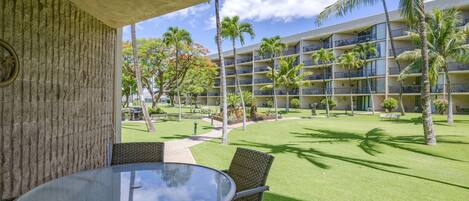 Un patio de hotel con área de comedor, palmeras y un edificio de varios pisos al fondo.