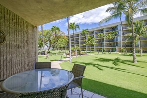 A hotel courtyard with a dining area, palm trees, and a multi-story building in the background. - Romanna’s Golden Ray Oceanfront Condo, Maui Resort (Kihei)