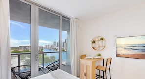 A balcony with a view of a cityscape and water, a dining area with chairs and a table, and a wall-mounted decorative item.