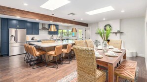 A modern kitchen with a central island, stainless steel appliances, and a dining area with wicker chairs and a wooden table.