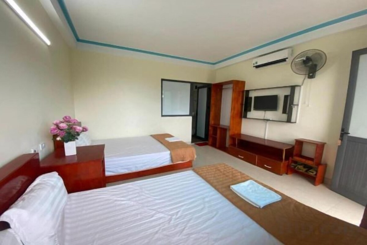 A hotel room with two beds, a desk with a chair, a TV, and a fan.