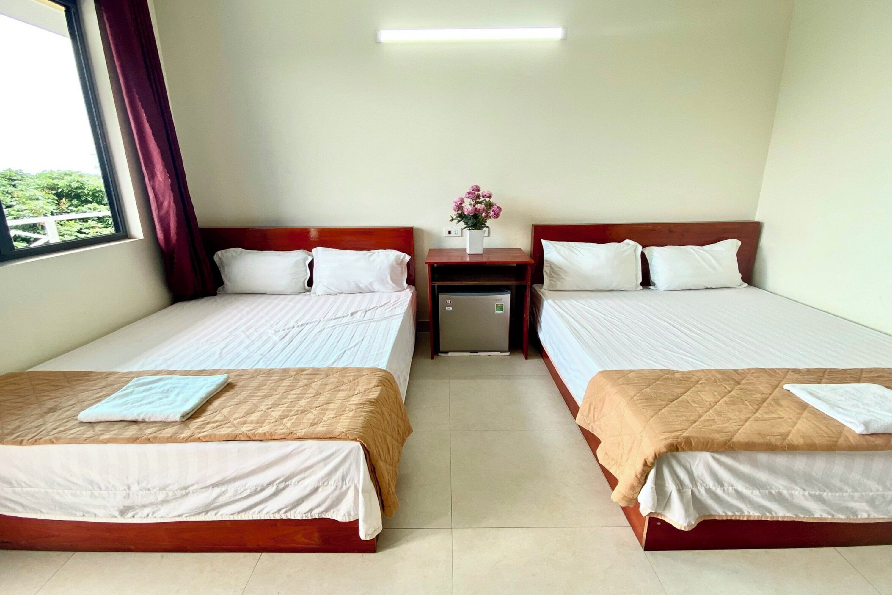 Habitación de hotel con dos camas, una mesita de noche, un refrigerador pequeño y una ventana con cortinas.