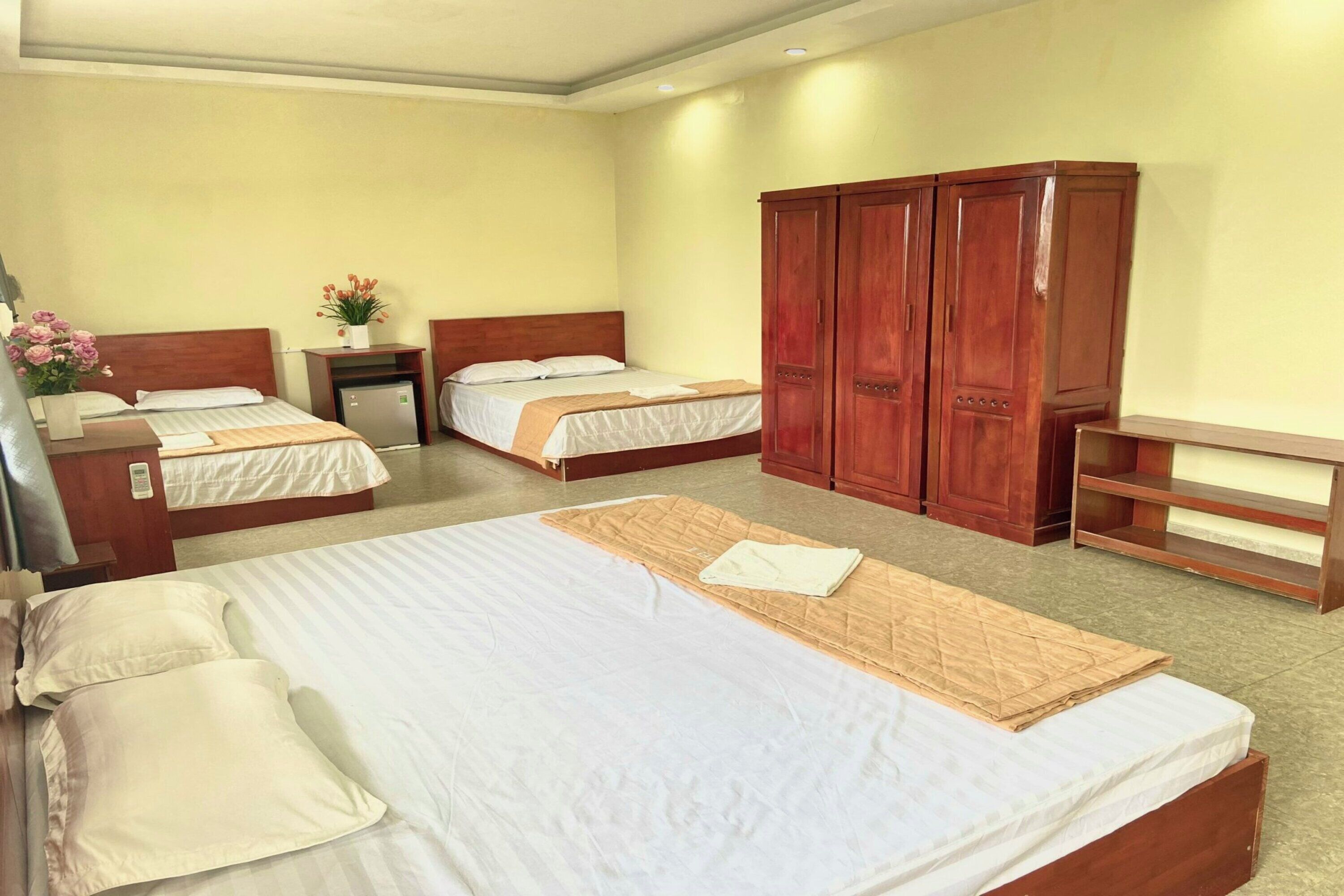 A hotel room with two single beds, a double bed, a wooden wardrobe, a bedside table, and a small desk.