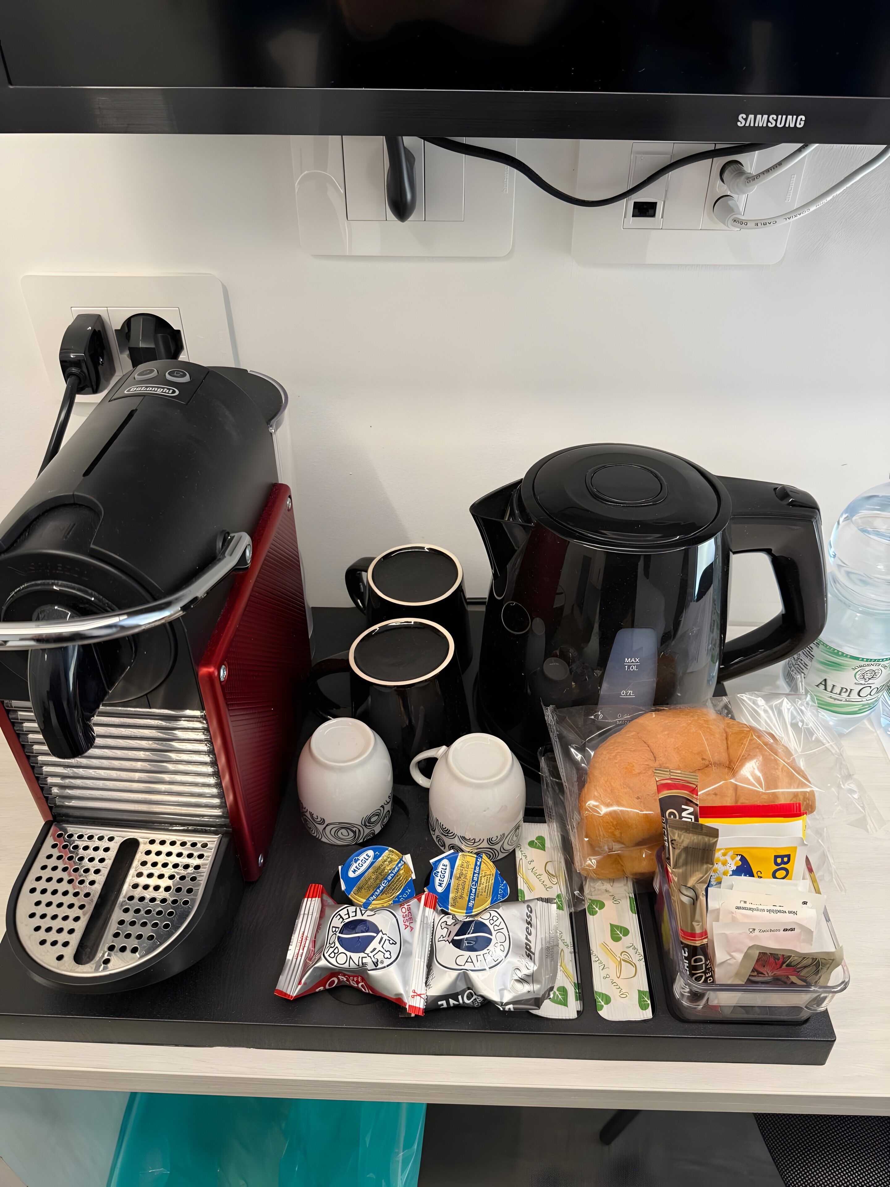 A coffee machine, two mugs, a kettle, a water bottle, and coffee pods on a counter.