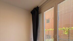 Una habitación con un sofá azul oscuro, ventanas amplias con persianas, una pared de ladrillo visible al exterior e iluminación en el techo.