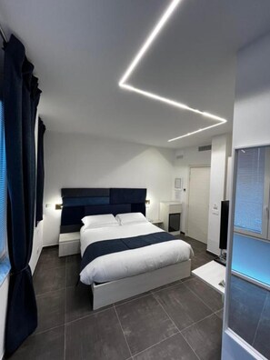A modern bedroom with a large bed, bedside tables, a flat-screen TV, and a built-in heater.