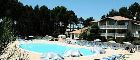 A swimming pool with lounge chairs and umbrellas, surrounded by a building with a balcony.