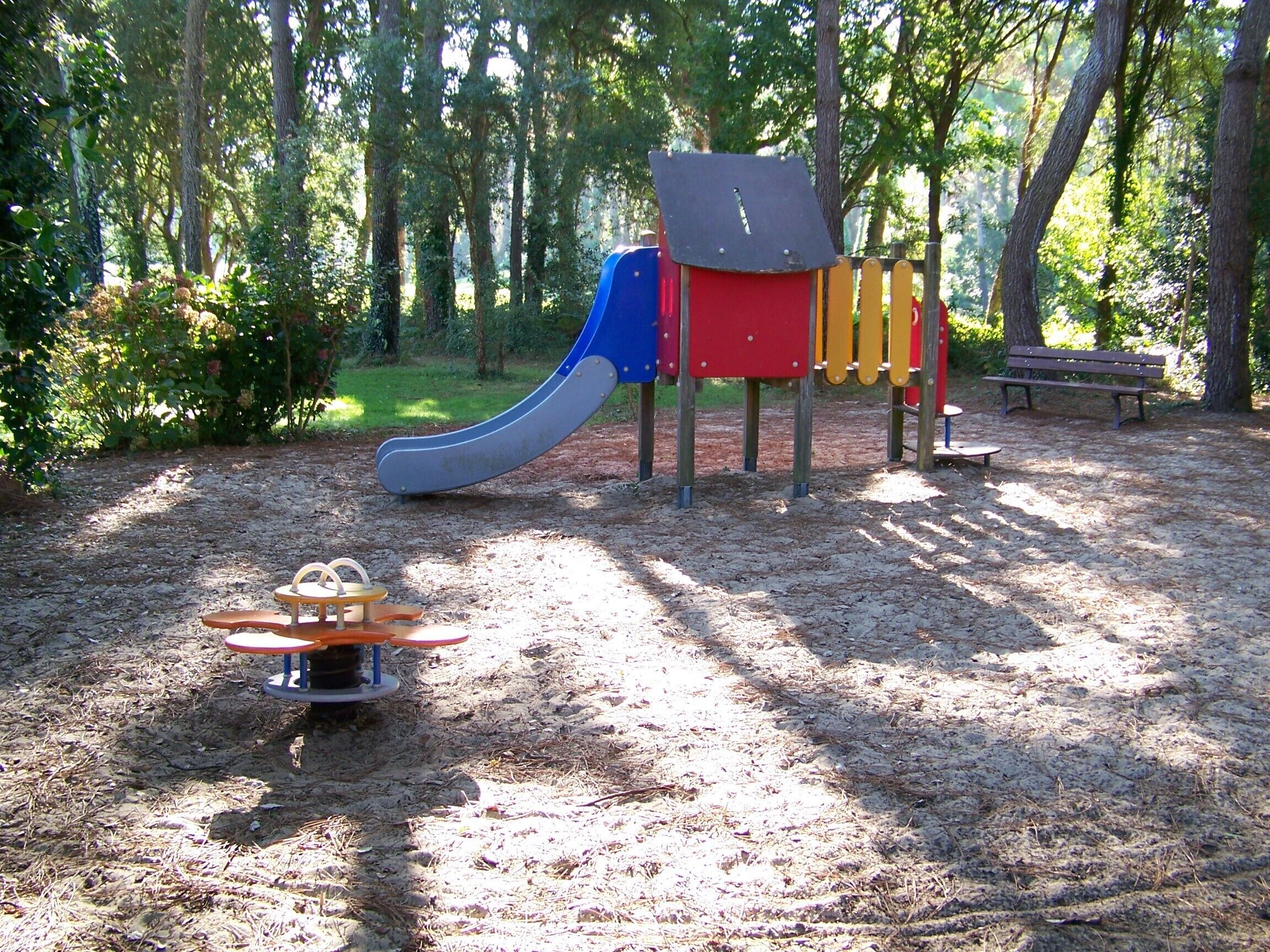 A playground with a slide, swings, and a bench in a wooded area.