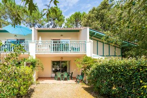Un edificio a due piani con un balcone, un patio coperto con sedie e un giardino curato.