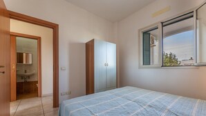 Un dormitorio con cama, armario, ventana con vistas y baño visible a través de una puerta abierta.