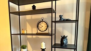 A black metal shelf unit with multiple shelves, each holding various decorative items including a clock, plants, and figurines. - Cosy Manchester House Near Etihad and Coop Live (Manchester)