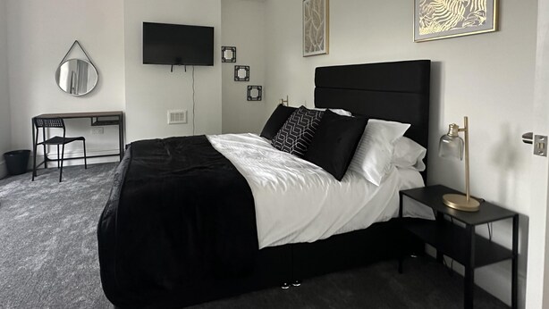 A modern bedroom with a black upholstered bed, a desk with a chair, a flat-screen TV, and artwork on the walls. - Cosy Manchester House Near Etihad and Coop Live (Manchester)
