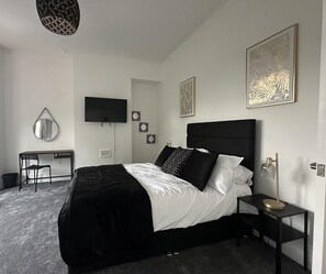 Ein modernes Schlafzimmer mit einem schwarzen möblierten Bett, einem Schreibtisch mit Stuhl, einem Flachbildfernseher und Kunstwerken an den Wänden.